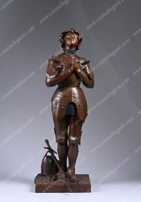 Joan of Arc at prayer wearing armor, with her helmet and sword at her feet