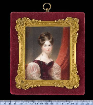 A Lady, seated in a red upholstered chair, wearing plum coloured dress with puffed white gauze sleeves, seed pearl brooch in the form of a bird at her corsage, pearl necklace, pendent pearl earrings and comb in her upswept hair, red curtain beyond.