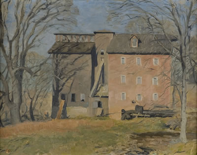 Red brick mill flanked by bare trees with water at right side.